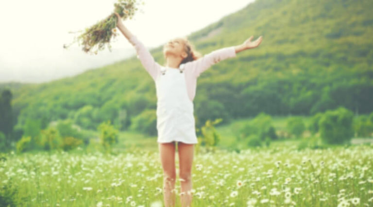 Criança no campo com folhes na mão erguendo os braços pro alto