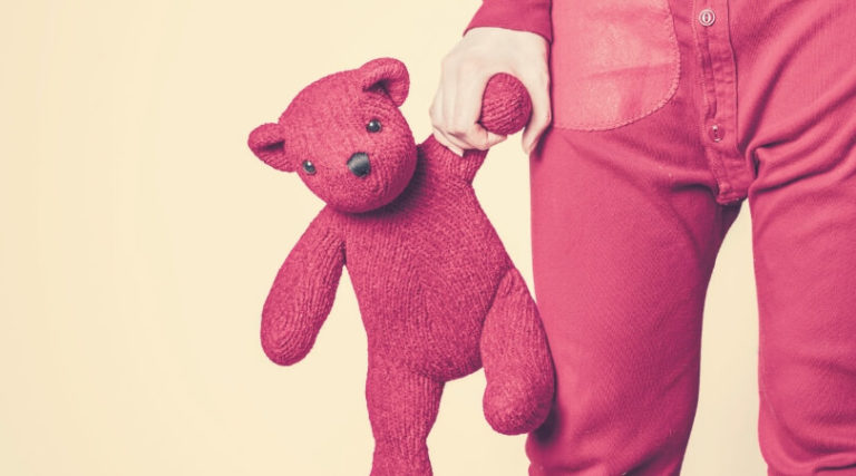 mão de criança segurando um ursinho de pelúcia vermelho