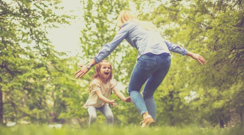 Mae e filha brincando de pega-pega em um lindo cenário verde em contato com a natureza.