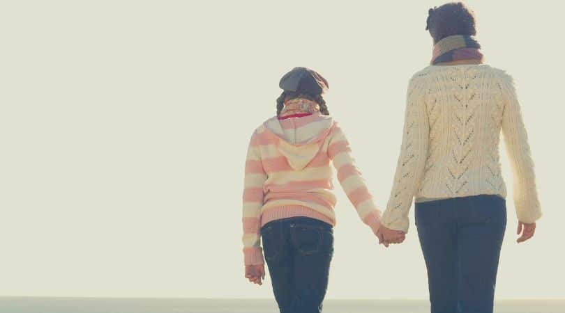 mae e filha de mãos dadas caminhando pela praia no pôr do sol.