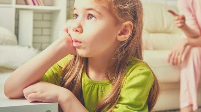 Criança de aproximadamente sete anos de idade, sentada com a mão apoiada no queixo com olhar expressando descontentamento.