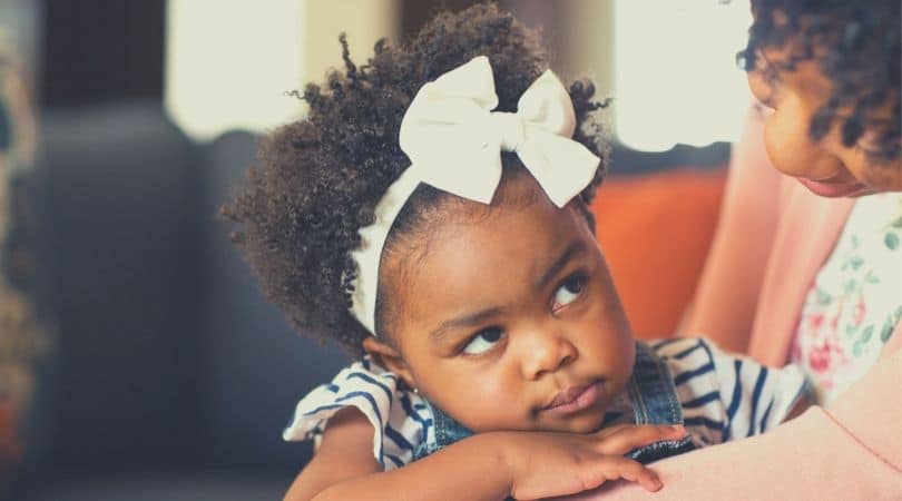 Mãe lançando um olhar carinhoso e acolhedor sobre a sua filha pequena de aproximadamente dois anos que está com um semblante mais sério